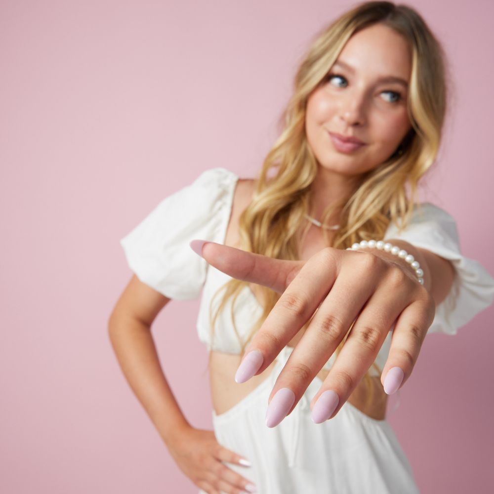 Girl wearing Instant Mani Co Velvet Pink Press on nails standing in front of pink background wearing white shirt 